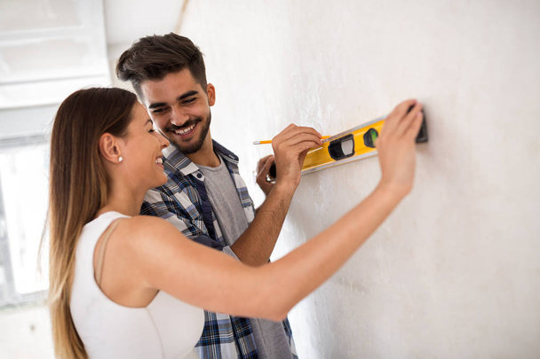 Smiling young couple measuring wall with level tool, renovation  - 写真・画像