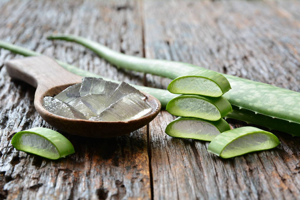 aloe gel on wooden spoon with aloe sliced on wooden table. - Photo, Image