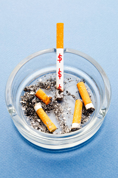 Зупинити палити - марнування грошей / доларів - з сигаретами та попільничкою на синьому фоні
 - Фото, зображення