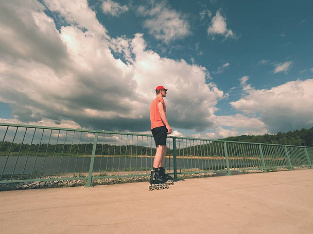 Vista traseira para patinador em linha em camiseta vermelha e calças pretas patinando na ponte. Patinação ao ar livre em linha
  - Foto, Imagem