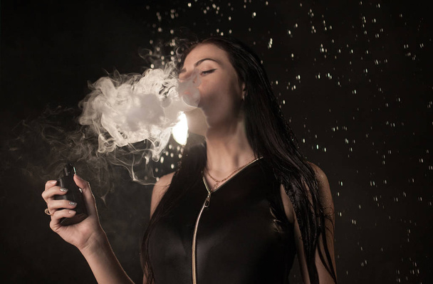 Young beautiful woman vaping e-cigarette. Water flowing on woman face. - Foto, afbeelding
