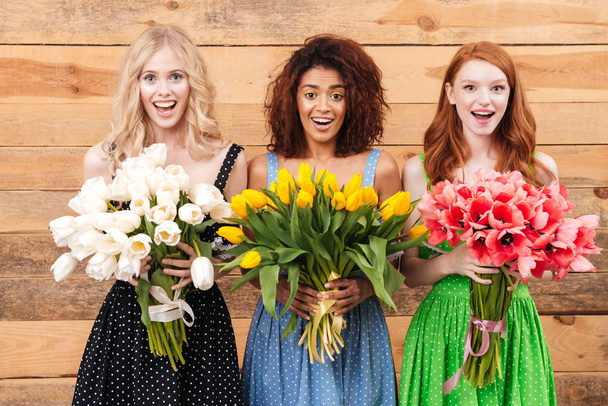 Three surprised women holding bouquets of flowers  - Foto, Bild