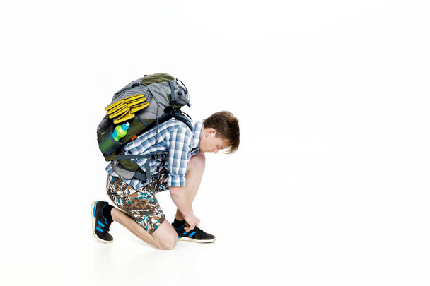 Young tourist with backpack ties up shoelaces on white background - Foto, Imagem