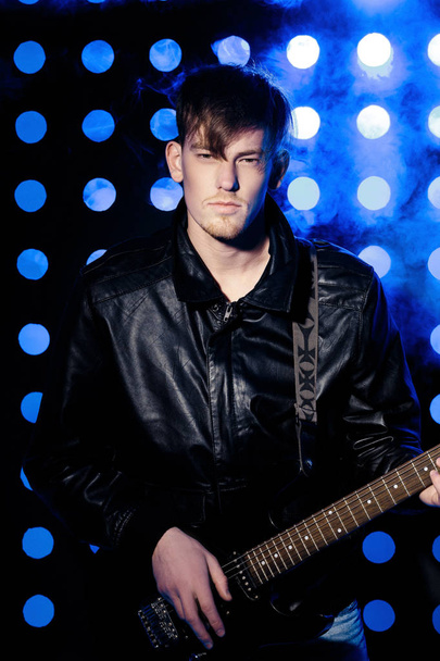 young attractive rock musician playing electric guitar and singing. Rock star on background of spotlights - Foto, imagen