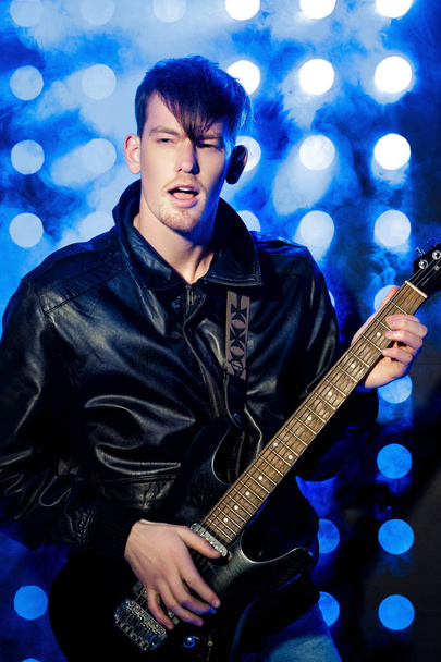 young attractive rock musician playing electric guitar and singing. Rock star on background of spotlights - Foto, Imagem