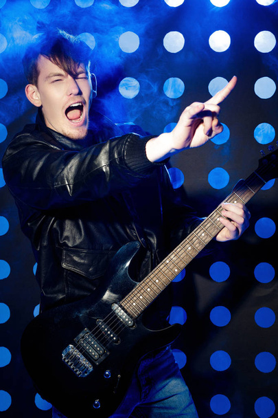 young attractive rock musician playing electric guitar and singing. Rock star on background of spotlights - Photo, image