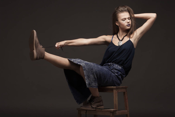 sexy fashion model with natural brunette hair, long legs, full lips, perfect skin, wearing brown shoes and long jeans skirt, sitting on floor, beauty photoshoot. Woman with creative make. - Фото, зображення