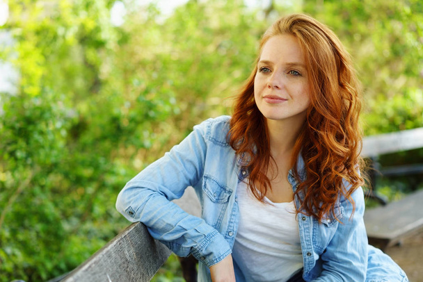 Thoughtful young redhead woman sitting on a bench - Foto, imagen