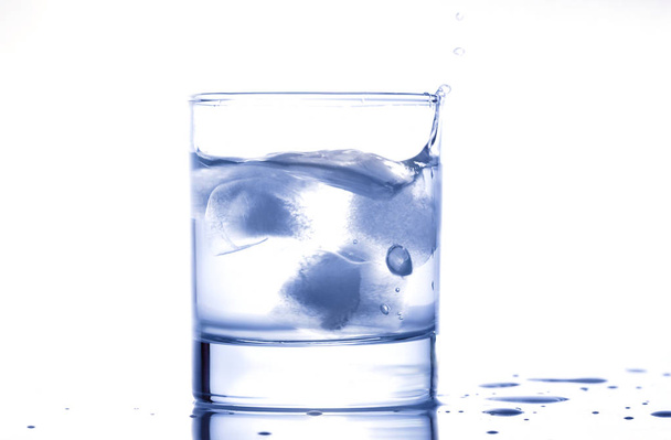 σταγόνες μπλε νερού που εκτοξεύεται από ένα ποτήρι με - Φωτογραφία, εικόνα