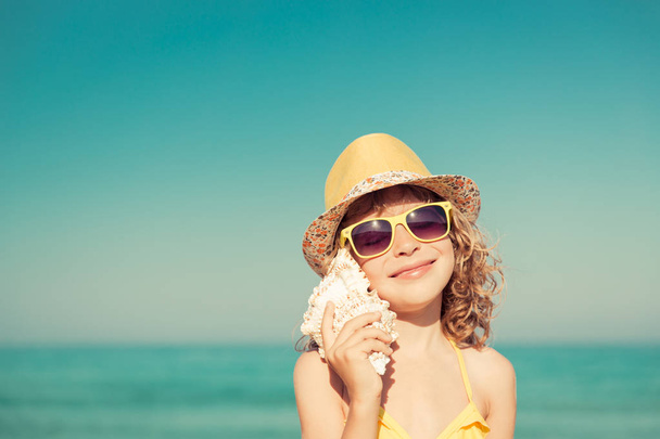 Boldog gyermek hallgatni seashell a strandon - Fotó, kép