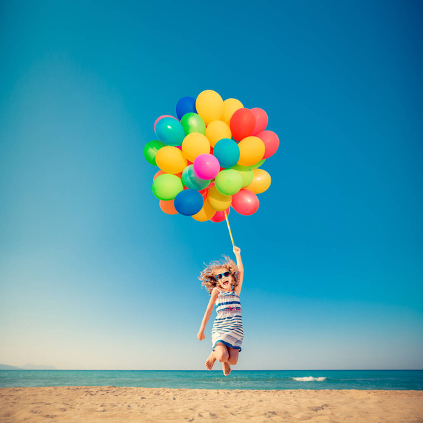 Happy child jumping with colorful balloons on sandy beach - Fotó, kép