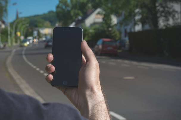 L'uomo sta tenendo e guardando il suo iPhone con una strada in background
 - Foto, immagini