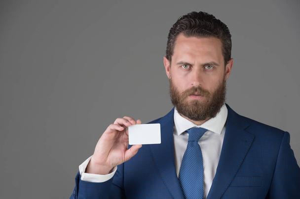 man holding white business card on grey wall background - Foto, afbeelding