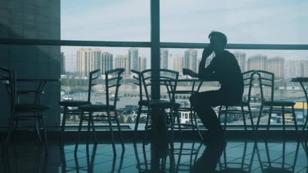 Junger Mann sitzt mit Smartphone allein am Tisch in Café in Einkaufszentren - Filmmaterial, Video