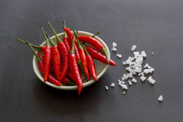 Punainen kuuma chili paprikat vihreällä lautasella, jossa on suolakiteitä lähellä mustalla pohjalla. Aasialaiset lajit
. - Valokuva, kuva