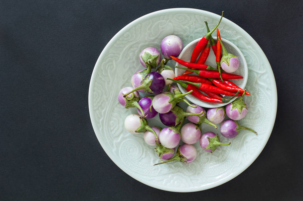 Paarse Thaise aubergines en hot chili peppers op een groene platen op een zwarte achtergrond. Aziatisch eten. - Foto, afbeelding