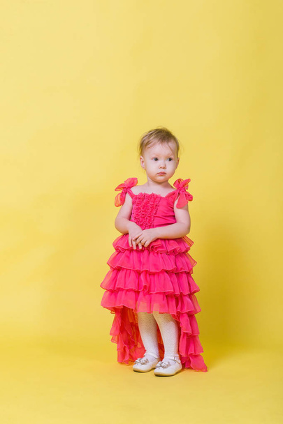 Girl toddler in a pink dress on a yellow background in the Studio - Zdjęcie, obraz
