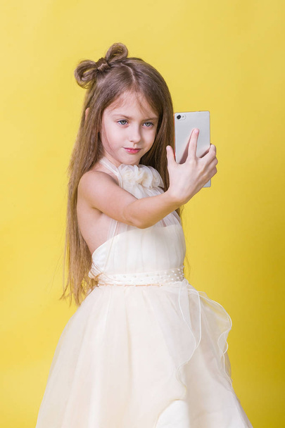 Teenager girl in a dress on a yellow background photographed themselves on the phone - Photo, image