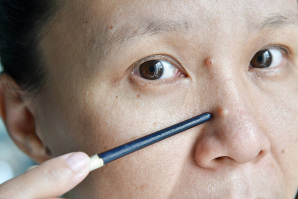 asiatico donna punto talpa su il suo faccia e naso
 - Foto, immagini