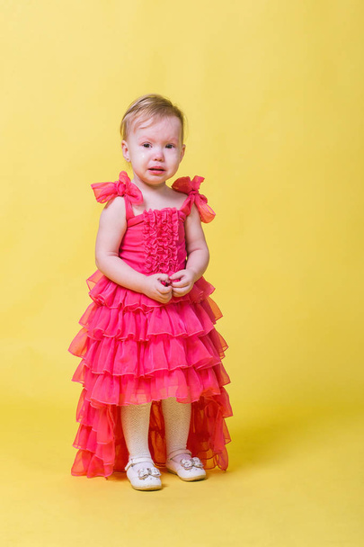 Girl toddler in a pink dress on a yellow background in the Studio - Foto, Bild