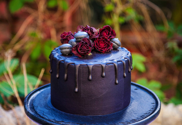 Gothic black rose cake on a wooden cake stand in a secret garden - Photo, Image