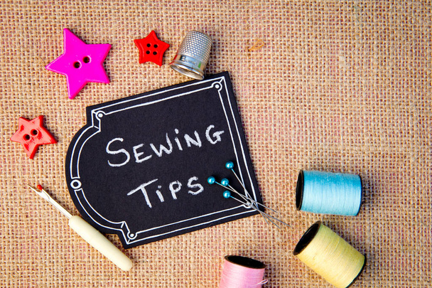 Consejos de costura en pizarra con botones, carretes de hilo de algodón y otros artículos sobre fondo de arpillera
 - Foto, Imagen