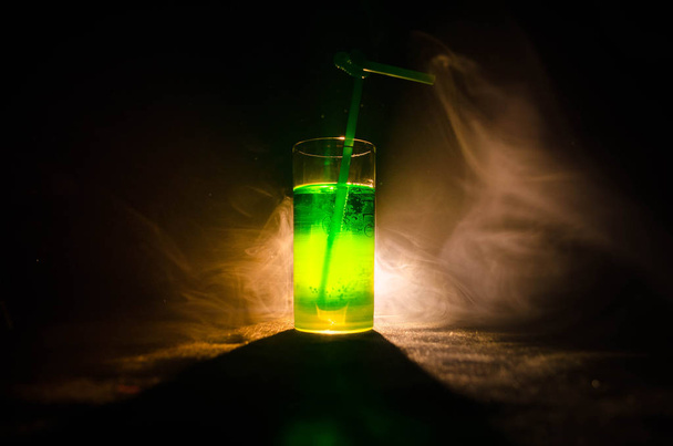 Стакан зеленого коктейля с соломой на темном фоне с дымом и подсветкой
. - Фото, изображение