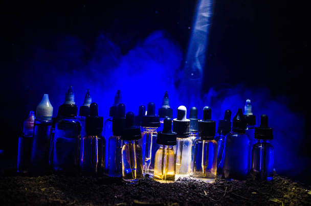 Концепція вейпу. Димові хмари та вейп-рідкі пляшки на темному тлі. Світлові ефекти
. - Фото, зображення