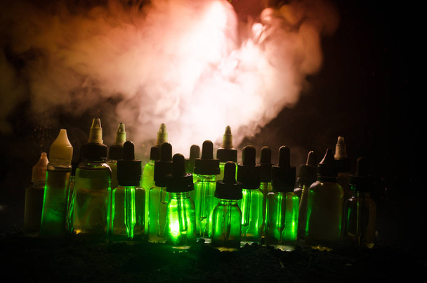 Vape concept. Roken wolken en vape vloeibare flessen op donkere achtergrond. Licht effecten. - Foto, afbeelding