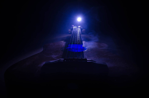Concepto musical. Guitarra acústica aislada sobre un fondo oscuro bajo haz de luz con humo con espacio de copia. Cuerdas de Guitarra, de cerca. Enfoque selectivo. Efectos de fuego
 - Foto, imagen