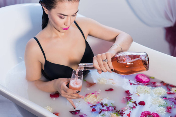 Seksowna brunetka kobieta nalewanie szampana w kąpieli - Zdjęcie, obraz