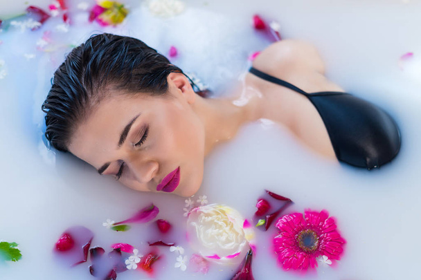 Femme brune sexy se détendre dans un bain de lait chaud avec des fleurs
 - Photo, image