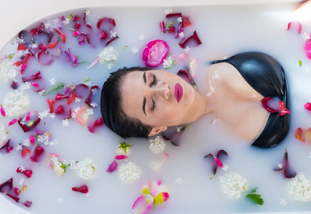 Sexy brunette woman relaxing in hot milk bath with flowers - Photo, Image
