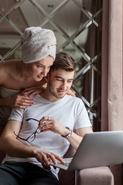 Young attractive couple looking at the laptop screen. Woman just after the shower. - Foto, afbeelding