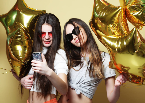 Two teenage girls friends with gold balloons  make selfie on a p - Foto, afbeelding