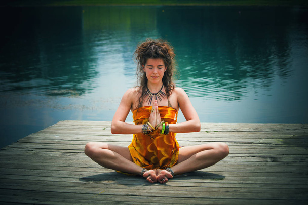 湖のほとりに瞑想的なヨガのポーズの女性 - 写真・画像