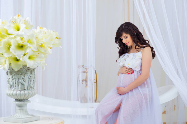 Gentle pregnancy. Beautiful pregnant in light white dress with orchids - Valokuva, kuva