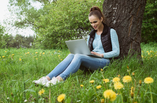 Молодая женщина с ноутбуком в парке - Фото, изображение