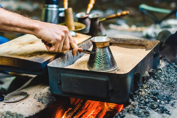 El hombre está cocinando café turco en la caja con arena bajo carbones vivos
 - Foto, imagen