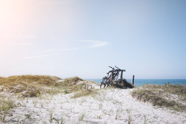 ドイツ北部のバルト海のビーチで草の覆われて砂丘に木製フェンスで駐輪されている自転車 - 写真・画像