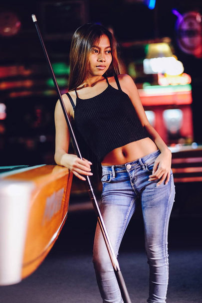 Nuori kaunis tyttö biljardibaarissa, jossa cue stick poseeraa
 - Valokuva, kuva