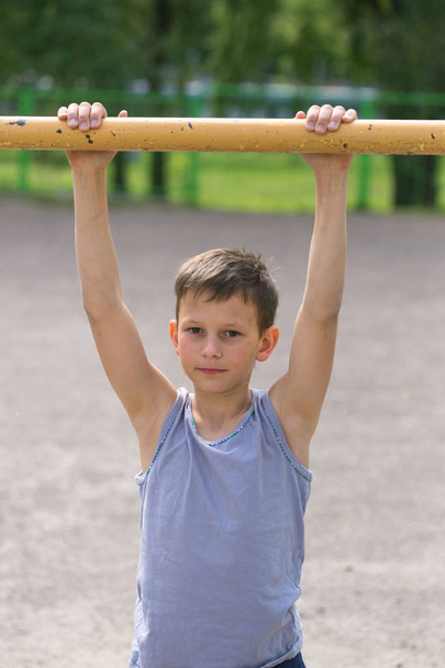 Een tiener in een T-shirt is betrokken bij het Turnen op een horizontale balk - Foto, afbeelding