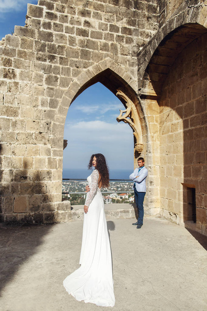 Bride in beautiful long gown walks to a groom along the ruins - Fotoğraf, Görsel