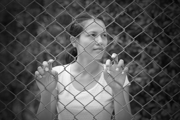 Outdoor asian woman look out with hand holding the steel mesh, Focus at her hands, black and white tone - Foto, Bild