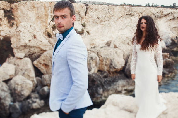 Stylish wedding couple stands between the rocks by the sea - Photo, image