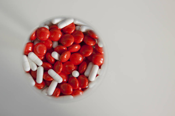 Red tablets and white pills in a glass on grey background - Фото, зображення
