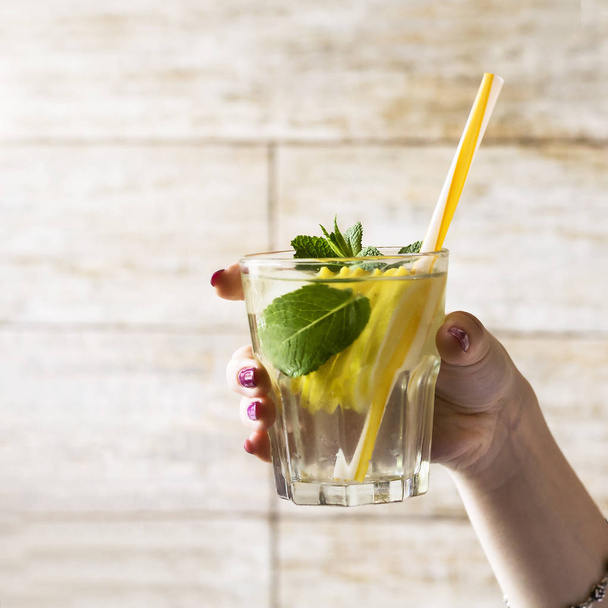 Un bicchiere di acqua disintossicante con un limone e foglie di menta fresca in mano a una ragazza. Stile di vita sano
. - Foto, immagini