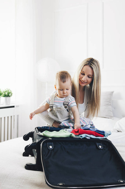 Travelling with kids. Happy mother with her child packing clothes for holiday - Фото, зображення
