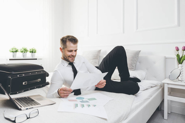 Businessman on bed working with a laptop from his hotel room - 写真・画像