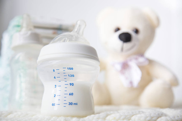Accessories for the baby. A stack of diapers with a bottle of milk and a teddy bear on a white background - Фото, изображение